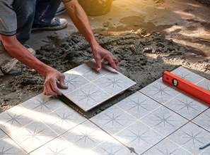 A worker installing concrete floor tiles or pavers by hand during an outdoor paving and construction process